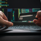 A pair of hands hold a credit card and type on a computer with a screen showing a wealth of data.